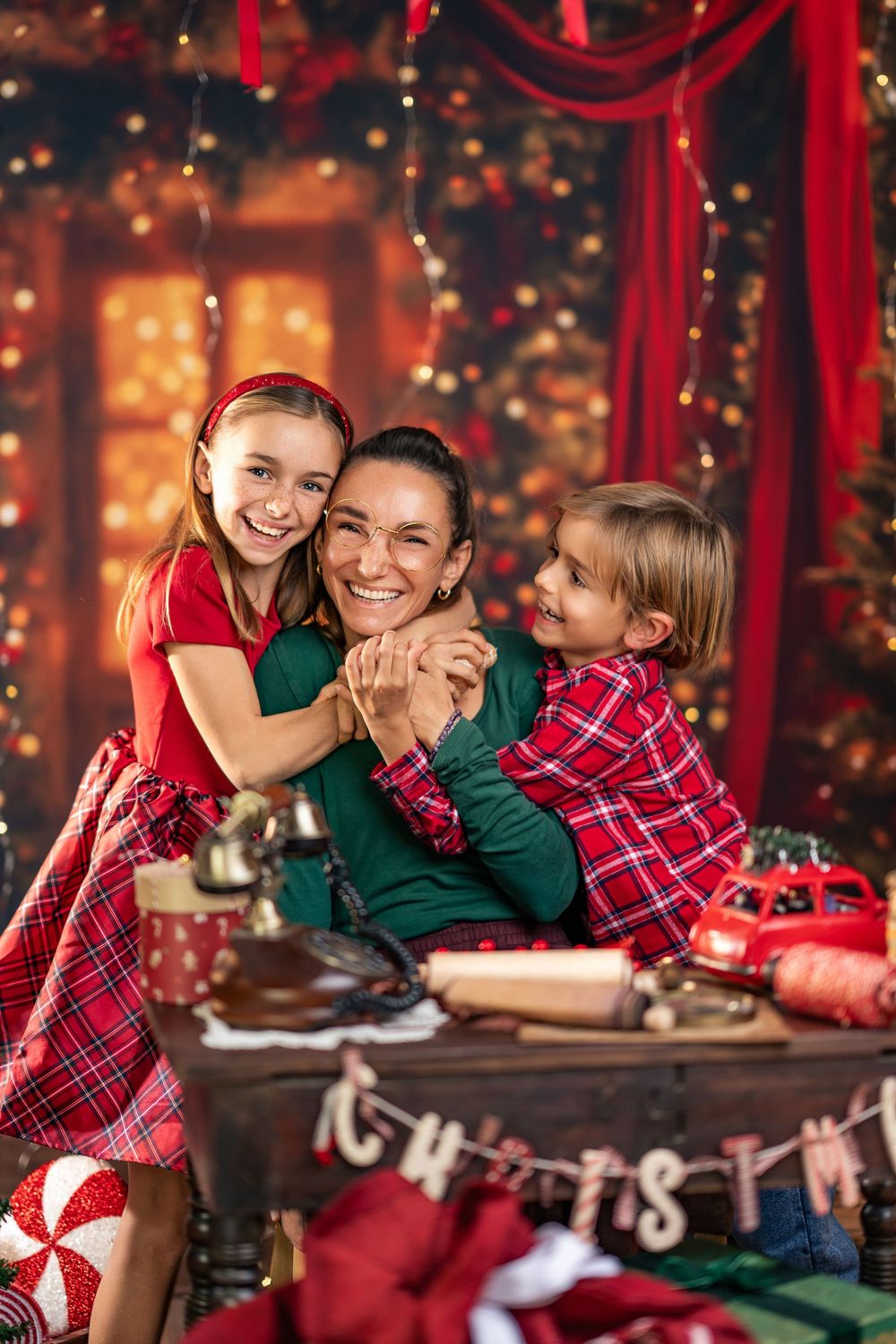 Family enjoying holiday moments together with festive red and green decor and twinkling lights in background.