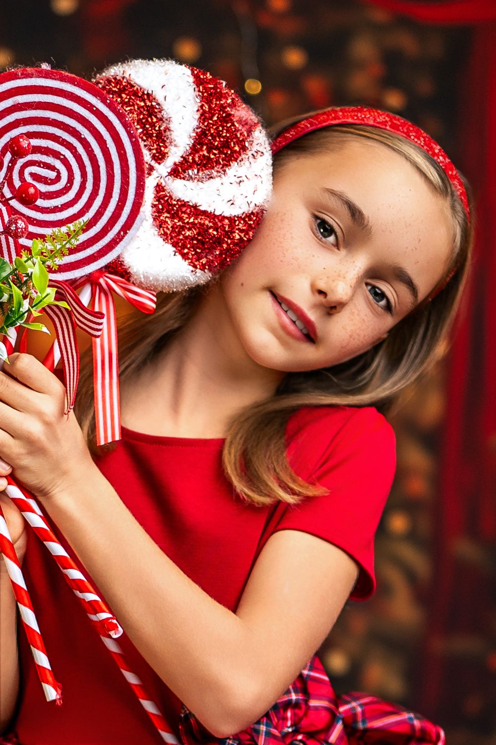 A festive holiday portrait with red and white candy canes and sparkly lollipop decorations against a warm bokeh background.