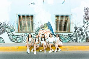 Group sitting together on a curb against a wall with artistic mural featuring flowing designs.