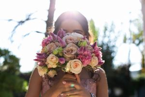 Sunlit bouquet of pink and peach roses held up against bright sky.