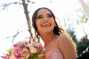 Joyful portrait in pink dress holding floral bouquet with sunlit backlight.