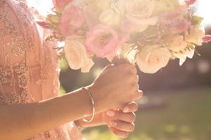Hands holding a romantic bouquet of pink and peach roses in golden sunlight.