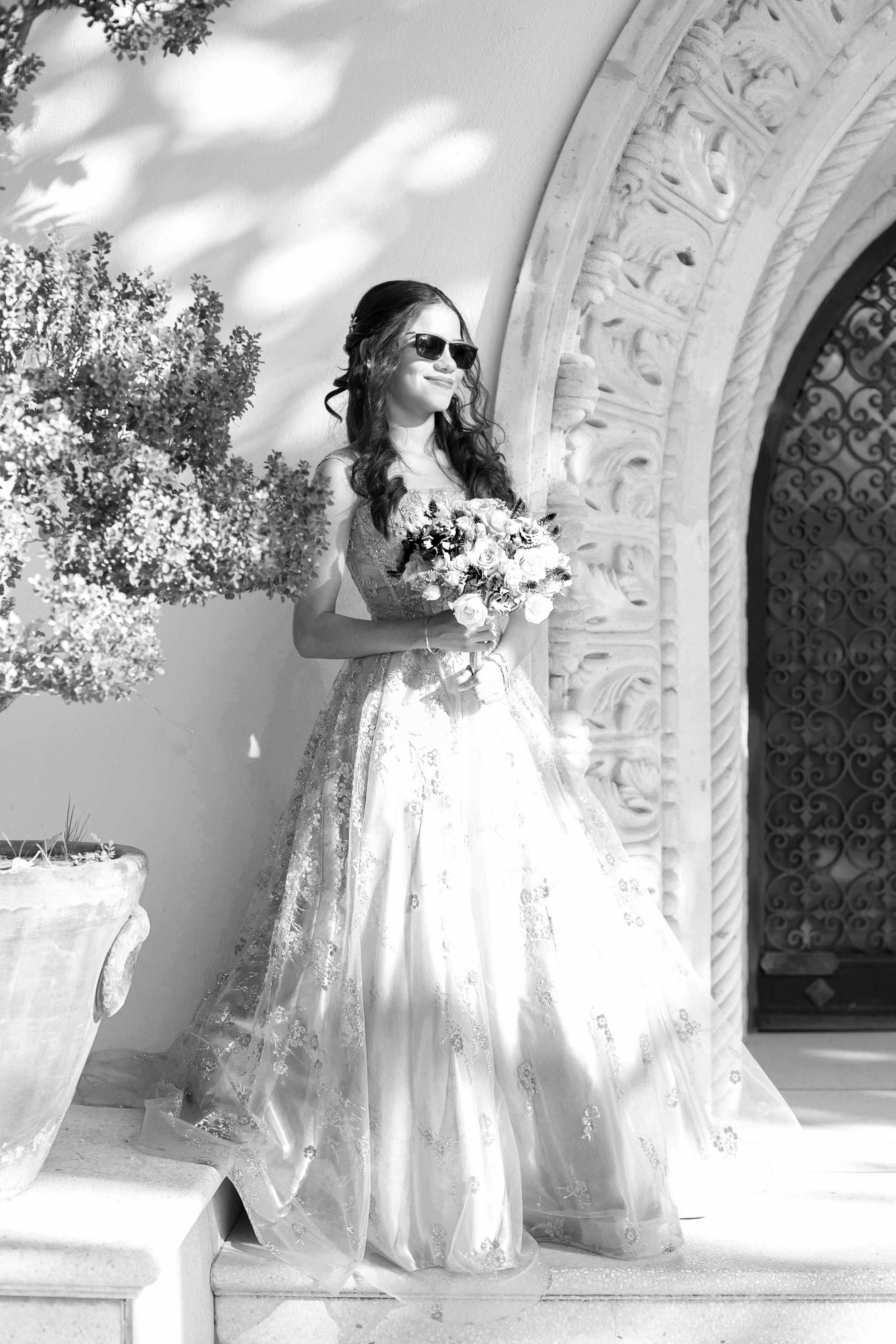 Black and white portrait of person in wedding dress posing by ornate archway.