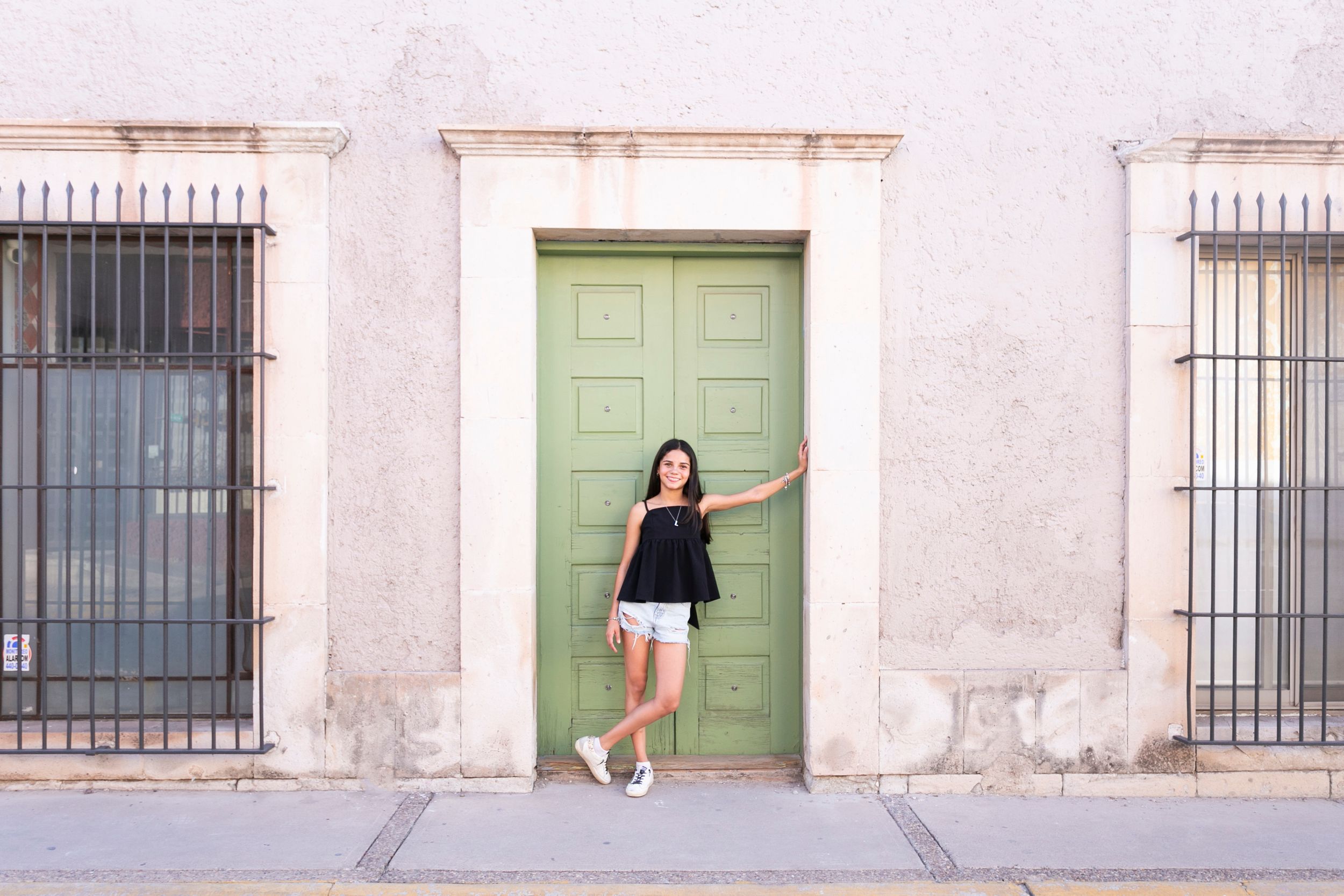Woman in casual outfit posing against mint green door and white wall.