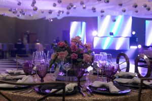 Elegant table setting with purple floral centerpiece and wine glasses under mood lighting.