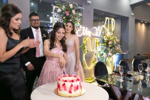 Wedding celebration with guests gathered around pink cake and neon sign decoration.