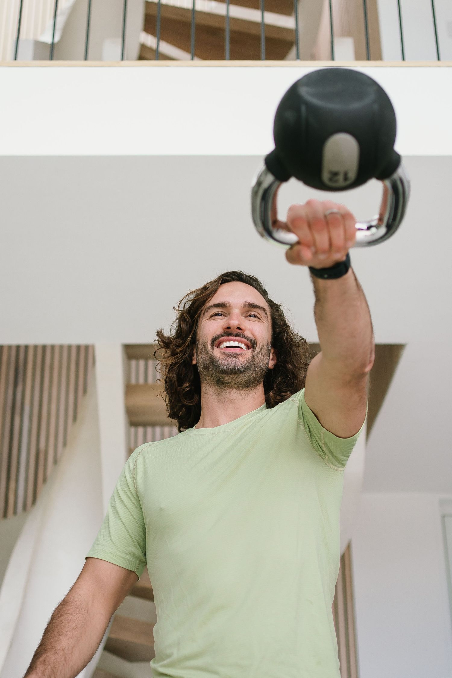 Person exercising with a kettlebell wearing a light green t-shirt in a bright interior space.