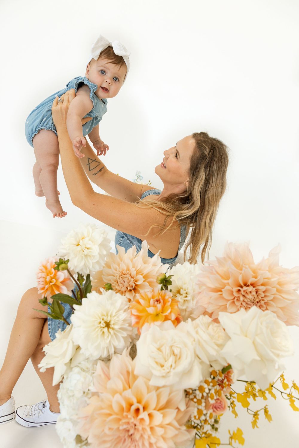 Playful moment with parent lifting baby up near peach and white flower arrangement.