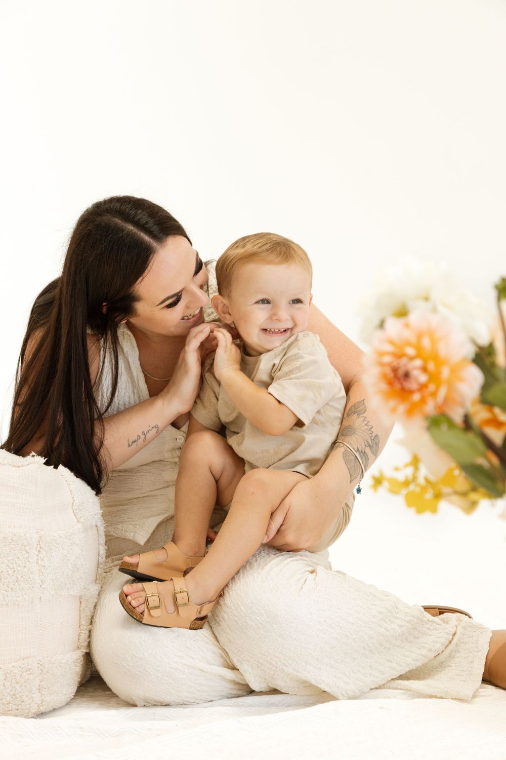Tender moment between mom and baby on white cushions with floral decor.