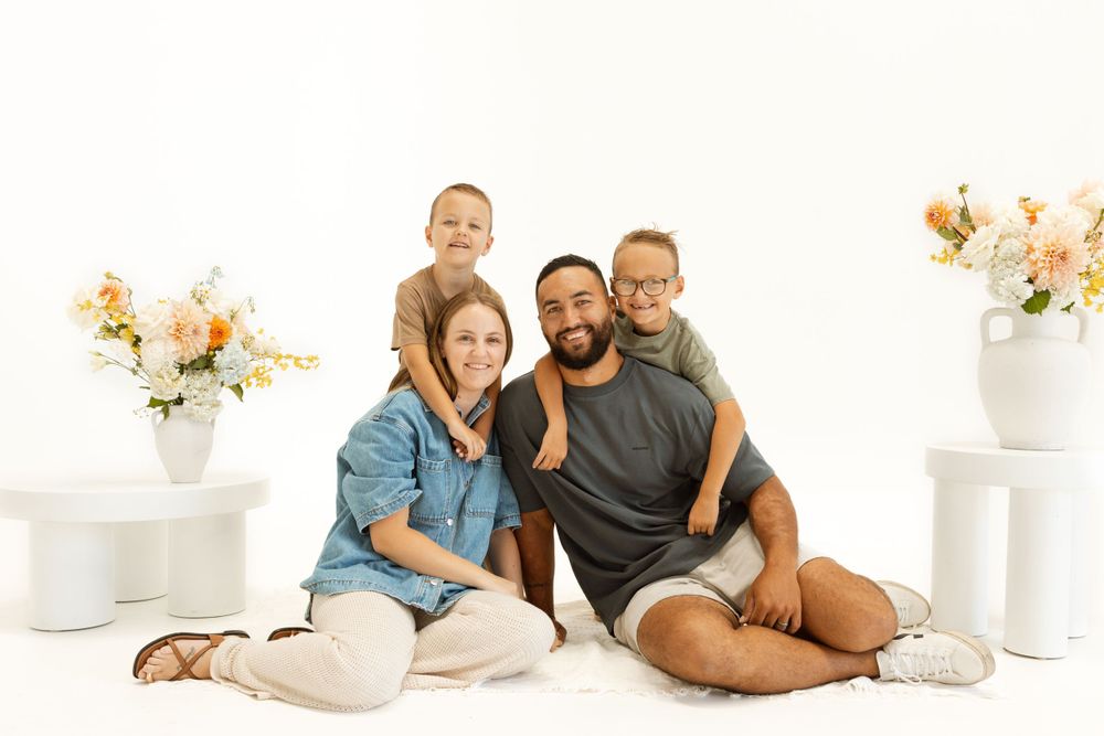 Family of four poses together on white backdrop with floral arrangements.
