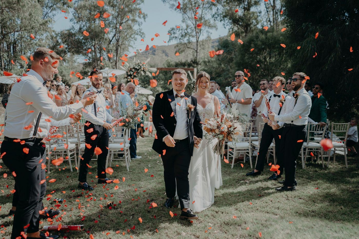 Wedding celebration outdoors with confetti flying through the air as guests gather in a garden setting.