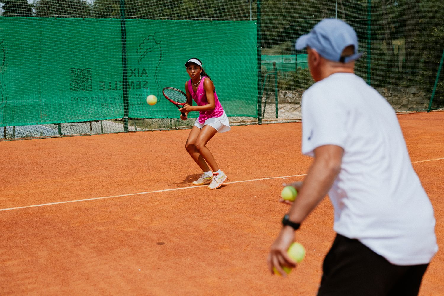 Tennis instructor giving lesson to player on clay court backdrop during daytime training session - CCTA Aix-en-Provence
