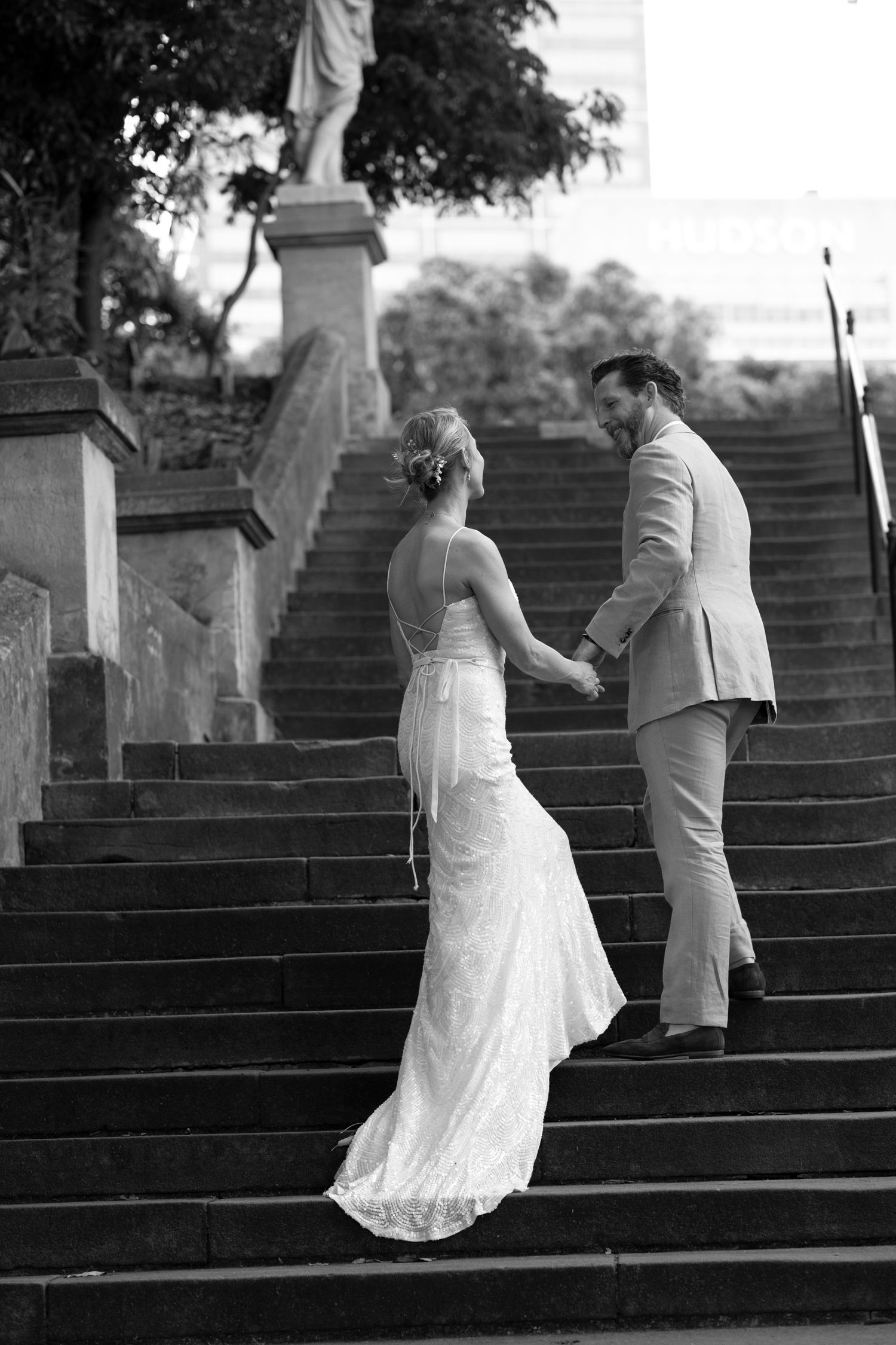 A vintage black and white photograph of a couple ascending elegant stone steps with a statue at the top.