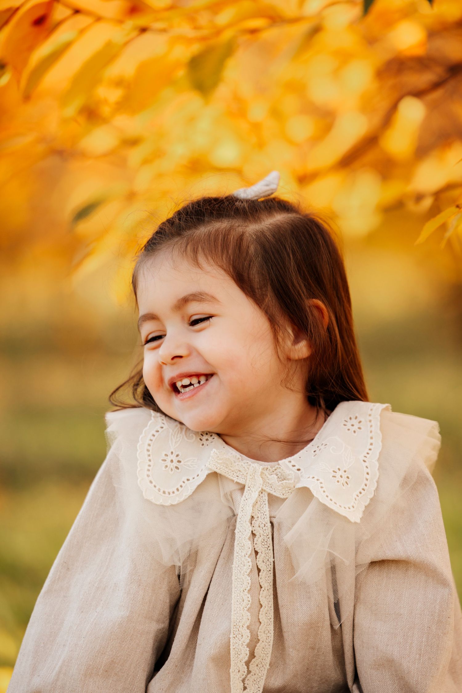 Joyful child in vintage-style dress laughing against golden autumn background.