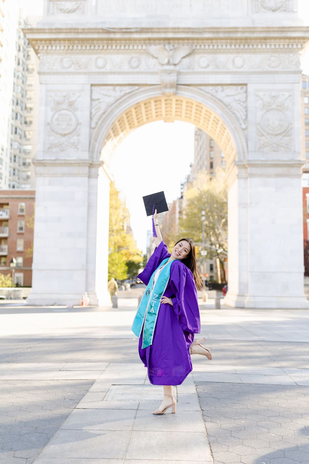 Graduate celebrating by tossing cap in air under Washington Square Arch.