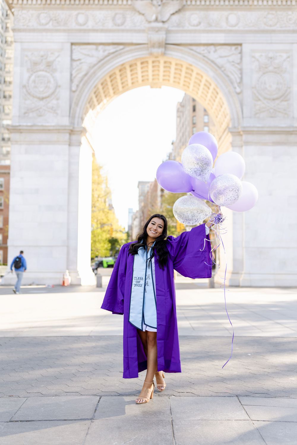 Graduate celebrating with purple balloons in front of Washington Square Arch.