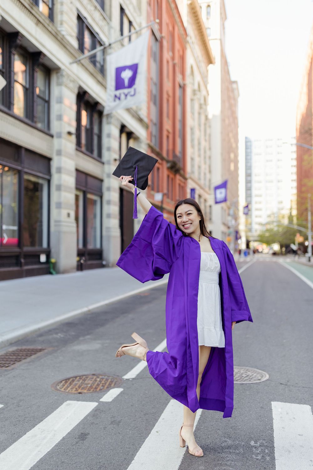 Graduate celebrating on campus street while holding graduation cap.