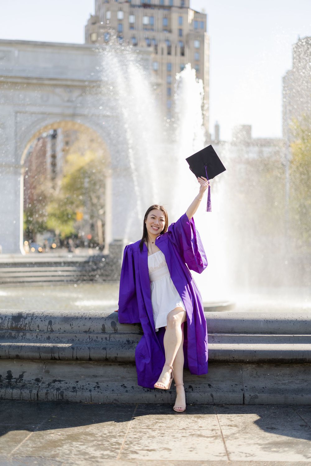 Graduate celebrating by fountain at Washington Square Park.