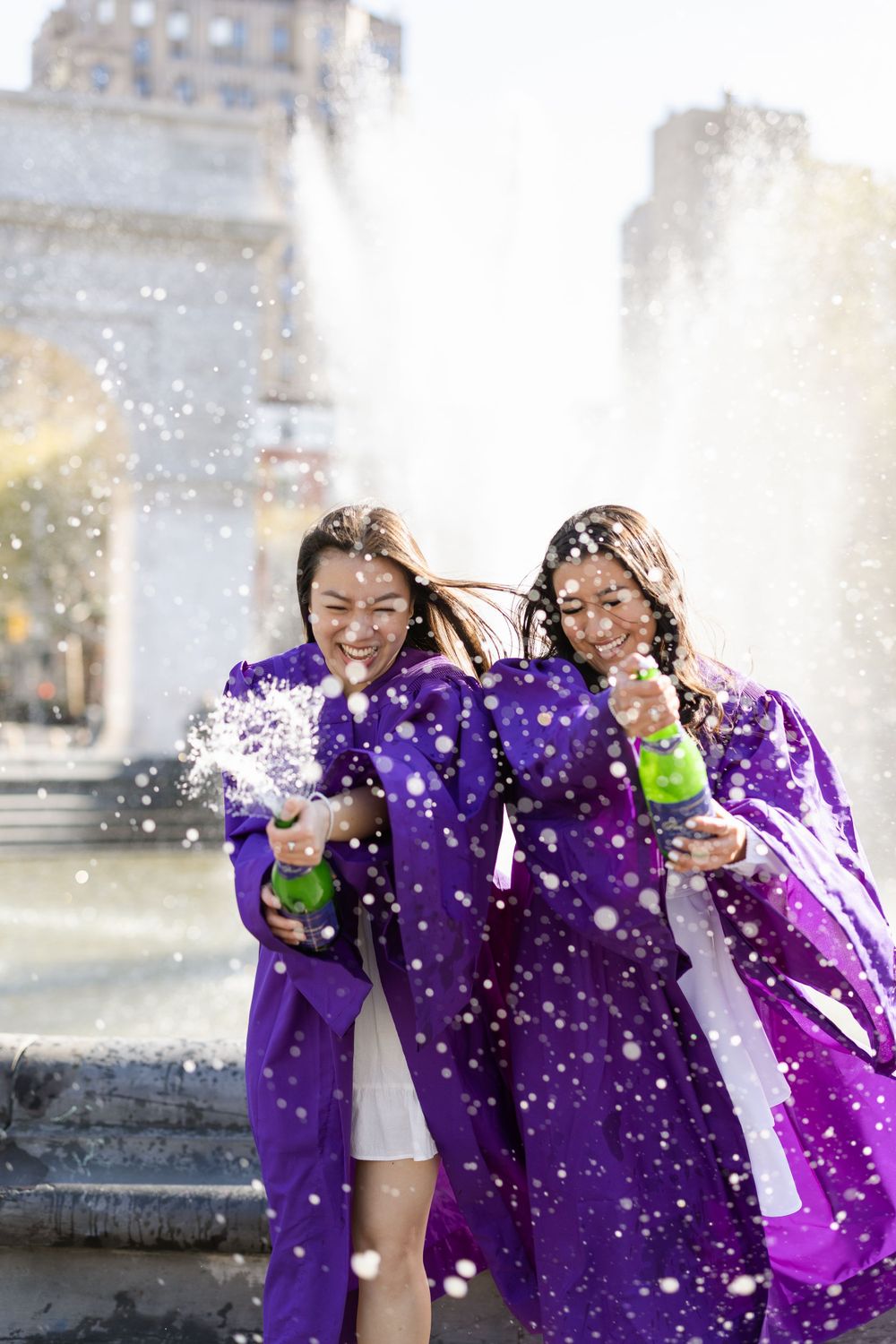 Graduates celebrate in purple robes getting splashed by fountain water.