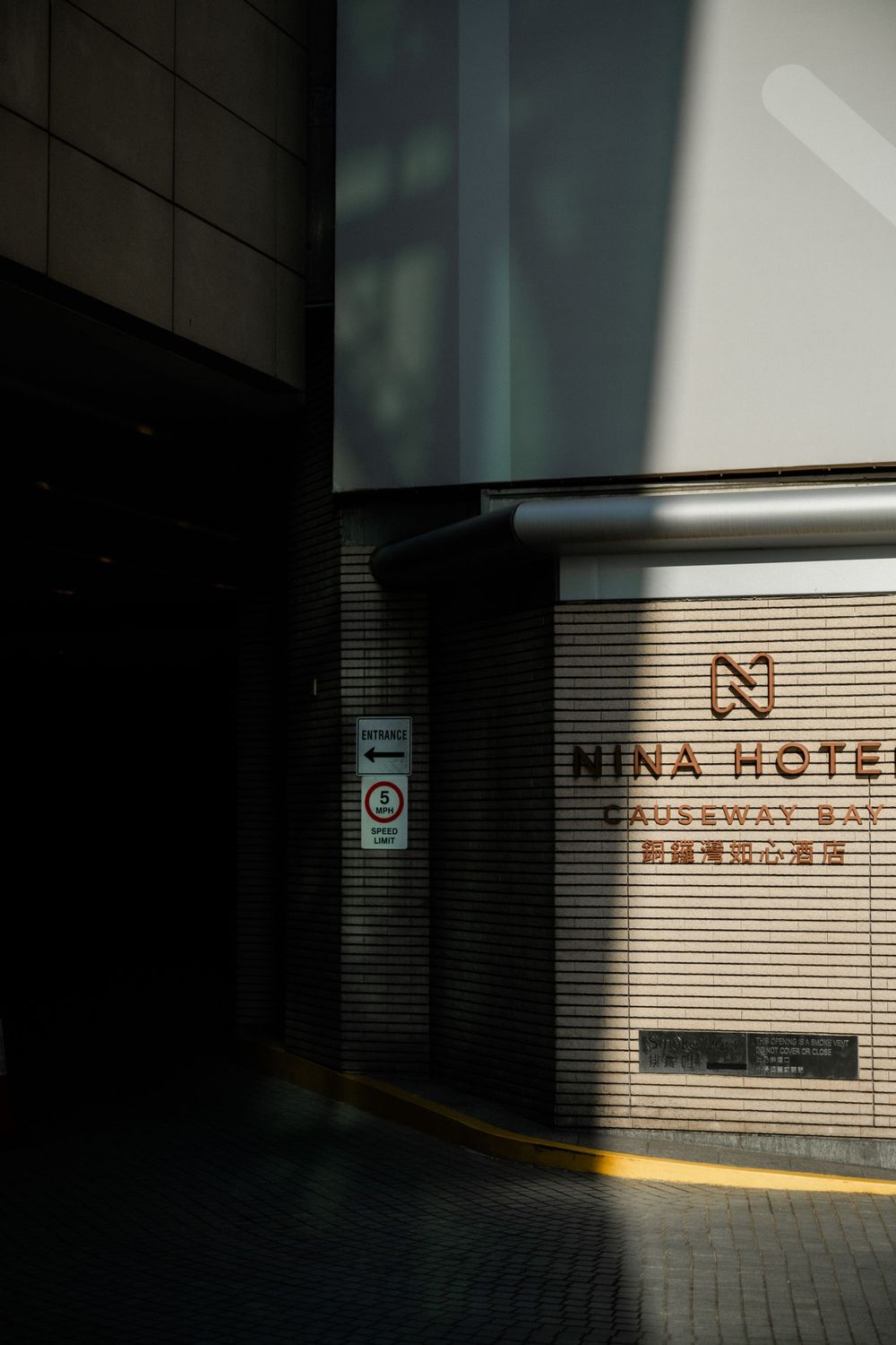 Exterior shot of Nina Hotel Causeway Bay entrance with dramatic shadow and light contrast on brick facade.