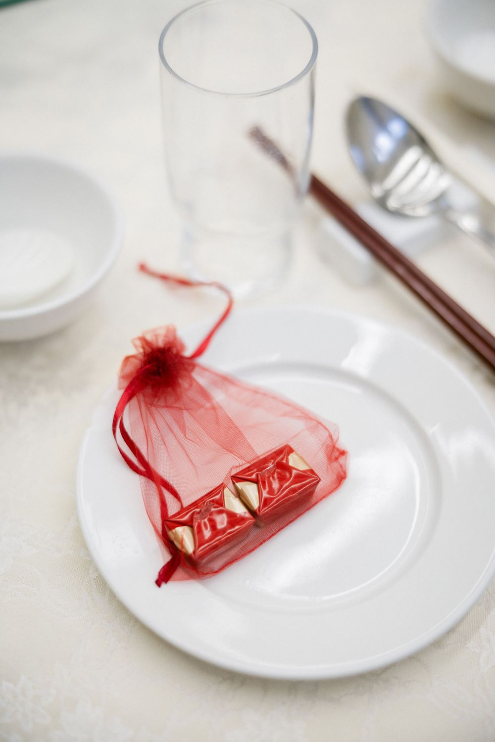 Red organza wedding favor bag with gold chocolates on white plate at reception table.