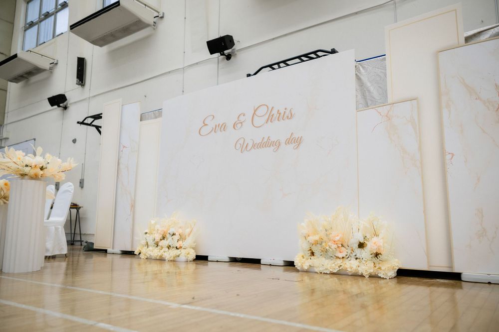 Wedding backdrop with floral arrangements reading Eva and Chris Wedding Day in hall.