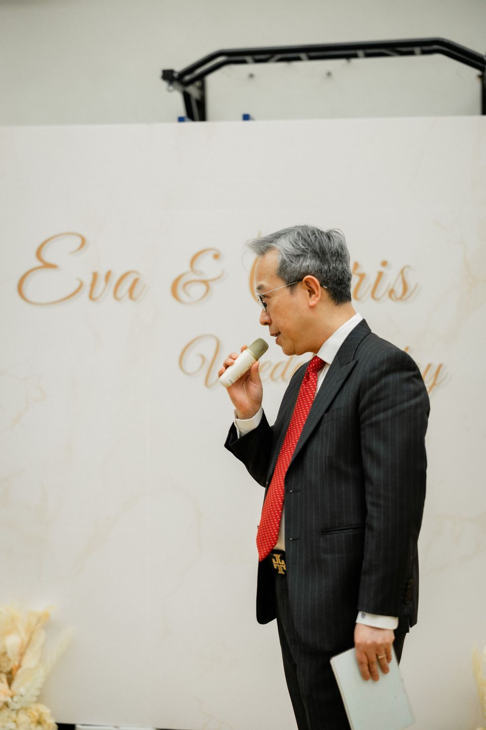 Man in pinstripe suit with red tie speaking at microphone at Eva and Chris wedding.