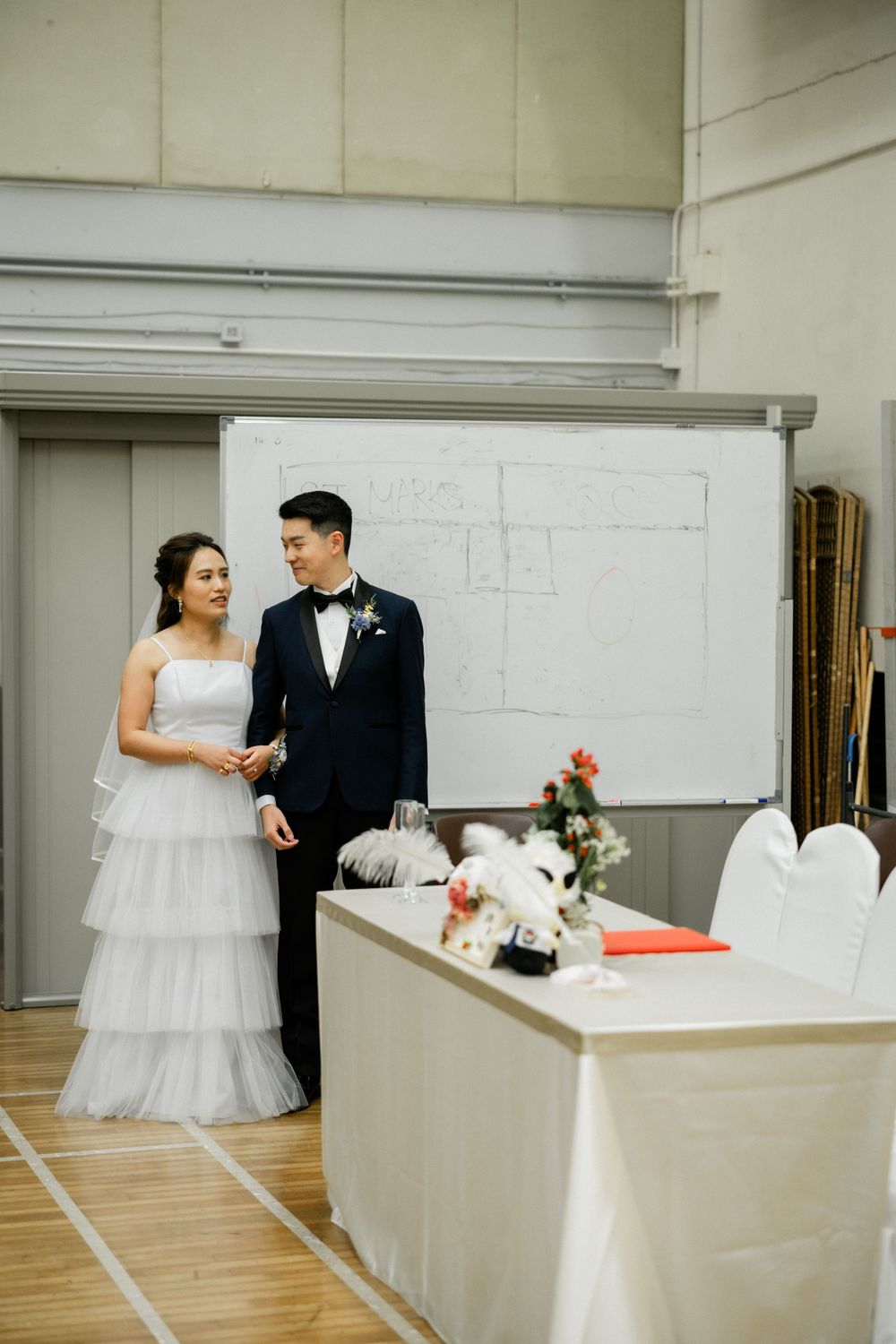 Bride and groom standing together at wedding ceremony in community hall venue.
