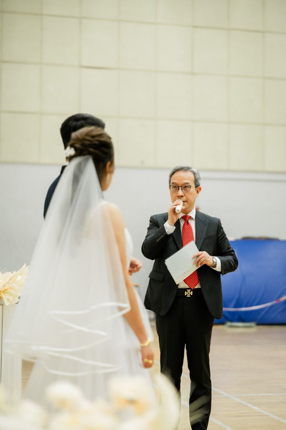 Wedding officiant in black suit reads from paper during outdoor bride and groom ceremony.