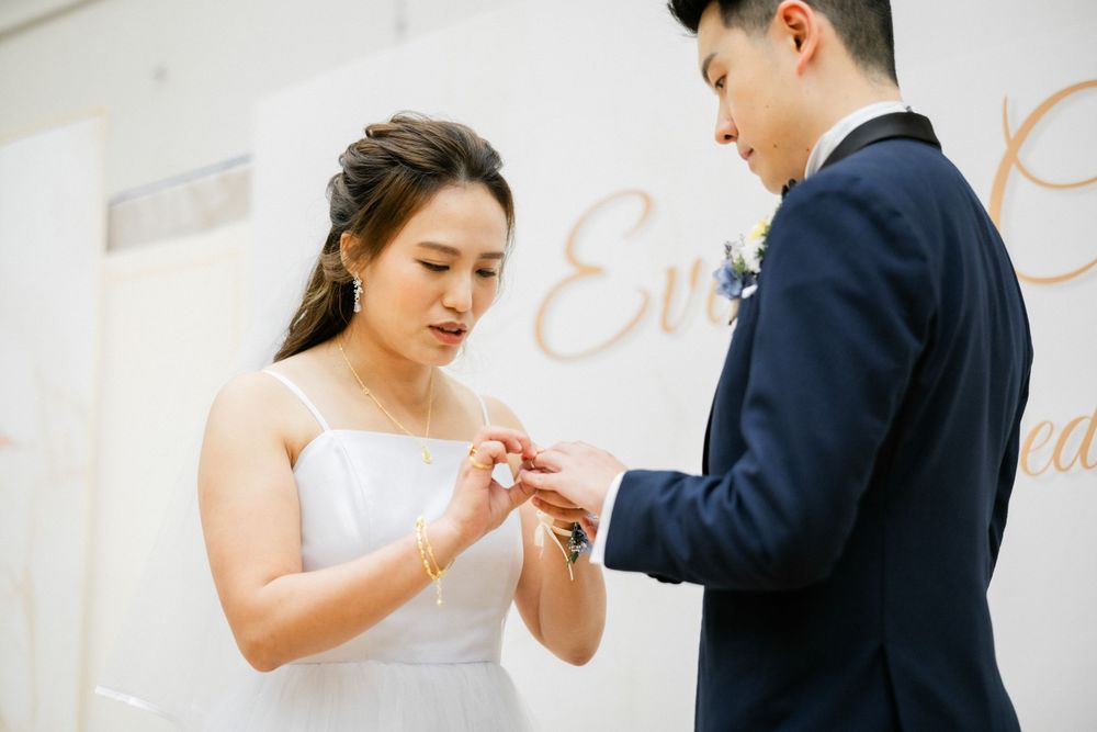 Bride places wedding ring on grooms finger during intimate ceremony at decorated venue.