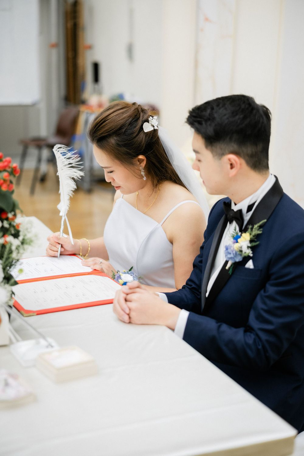 Bride signs wedding documents as groom watches attentively at their wedding ceremony table.