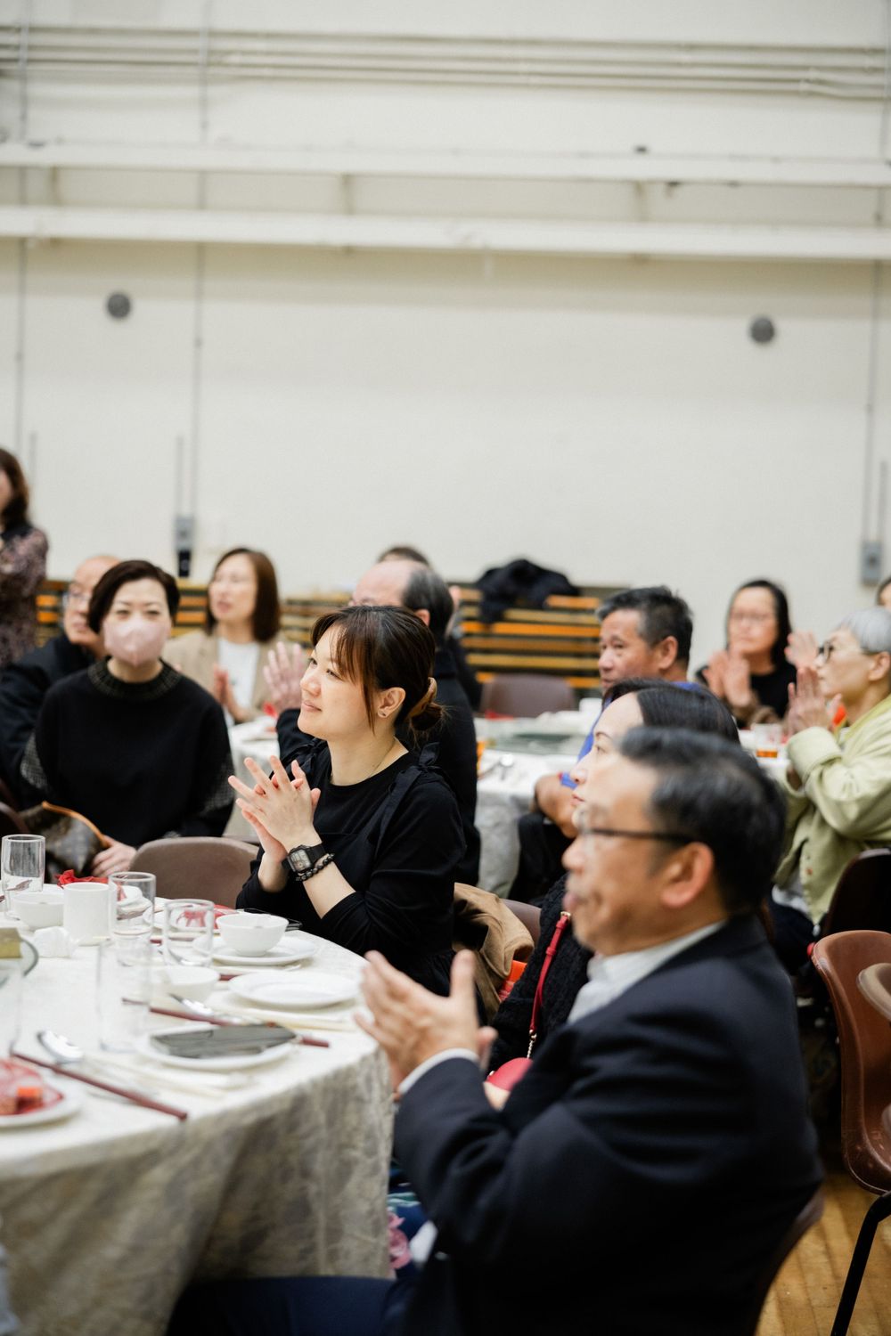 Wedding guests smile and applaud during a reception celebration at a banquet hall.