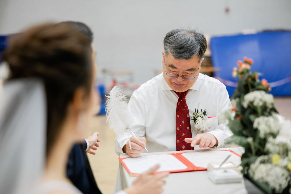 Older gentleman in white shirt and red tie signs official wedding documents at ceremony.