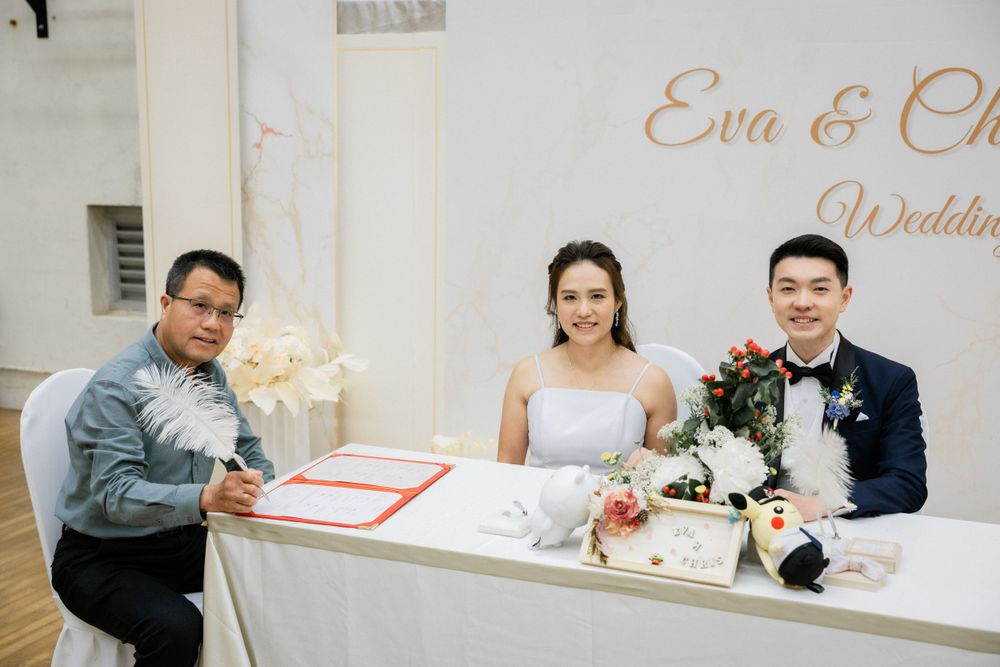 Bride Eva and groom Chris pose with a witness at their wedding signing table.