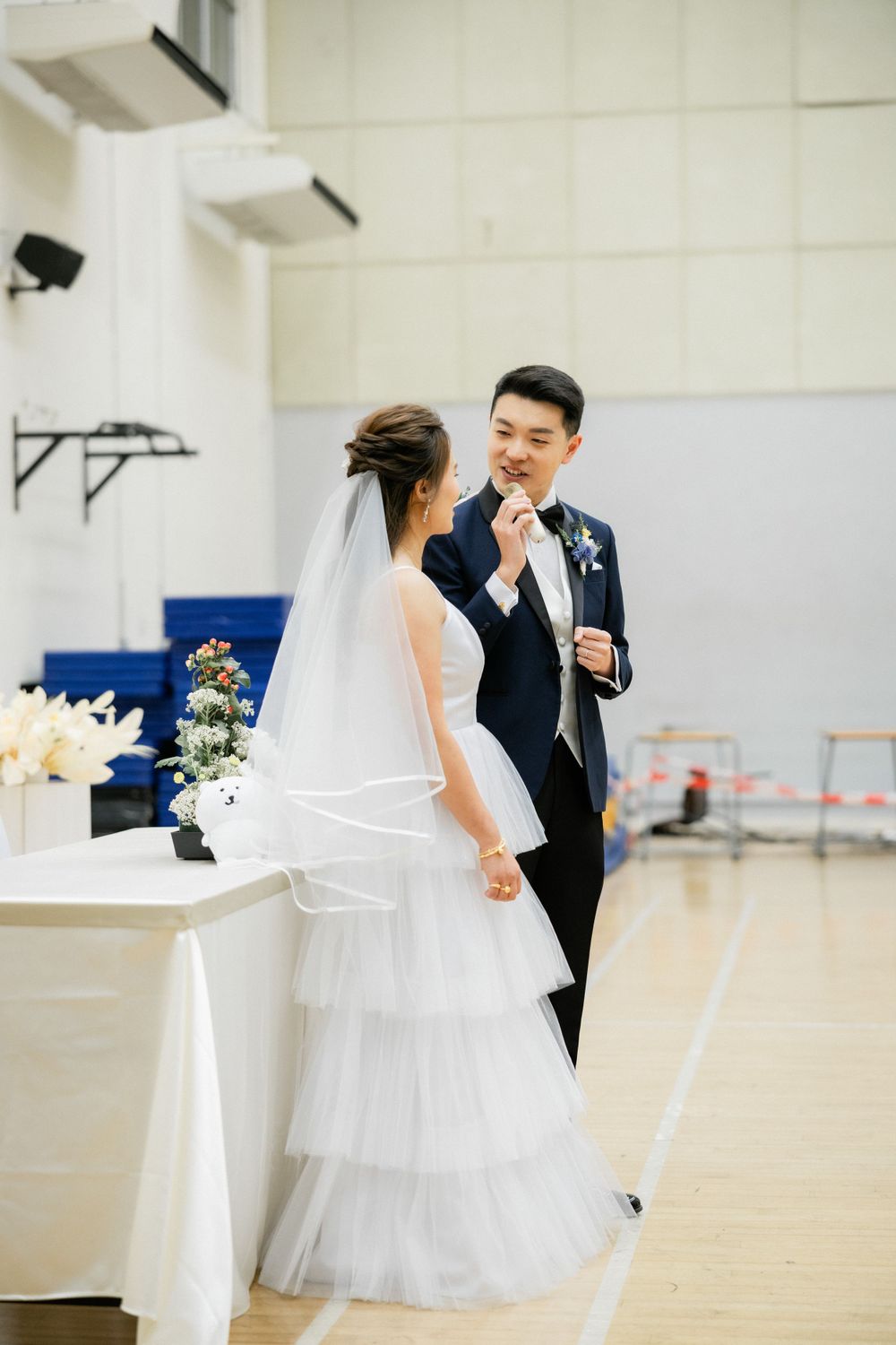 Bride in layered tulle gown with veil and groom in navy suit sharing a romantic moment.