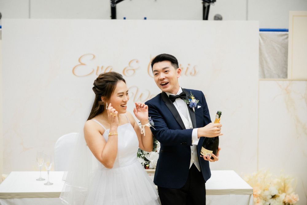 Bride and groom popping champagne bottle together at their wedding reception celebration.
