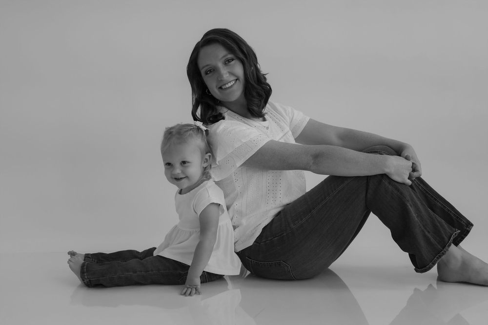 Black and white portrait of parent and child sitting together on white background.