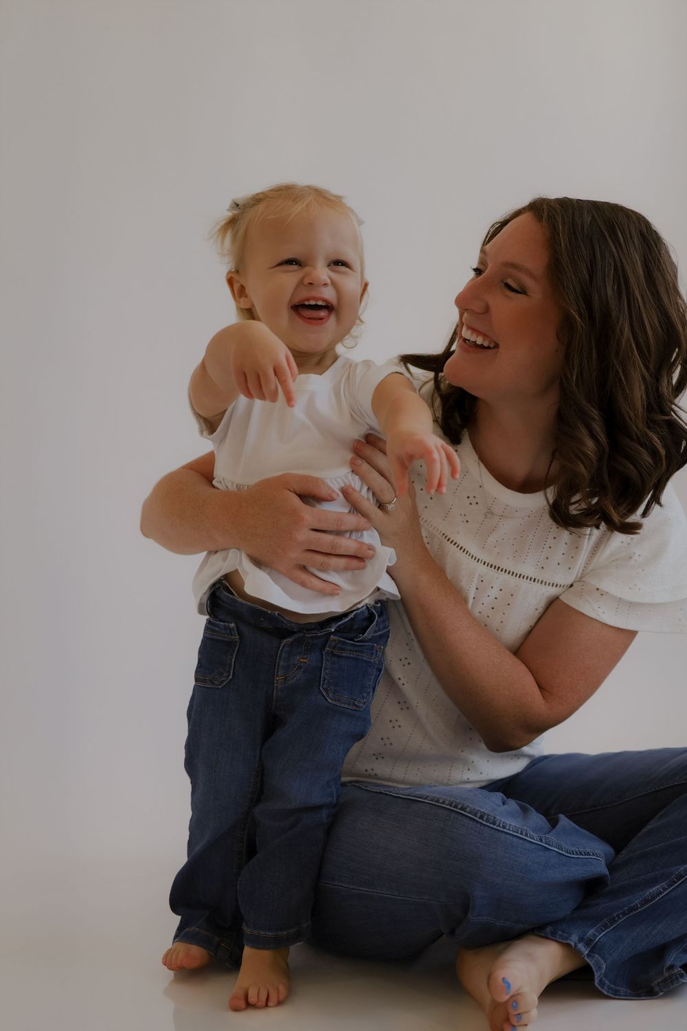 Candid moment of laughter between adult and toddler playing together on white background.