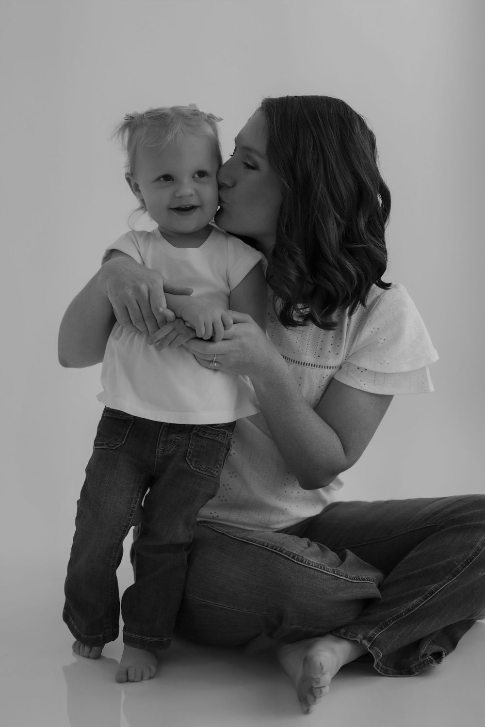 Black and white portrait capturing tender moment between adult and child on minimalist background.