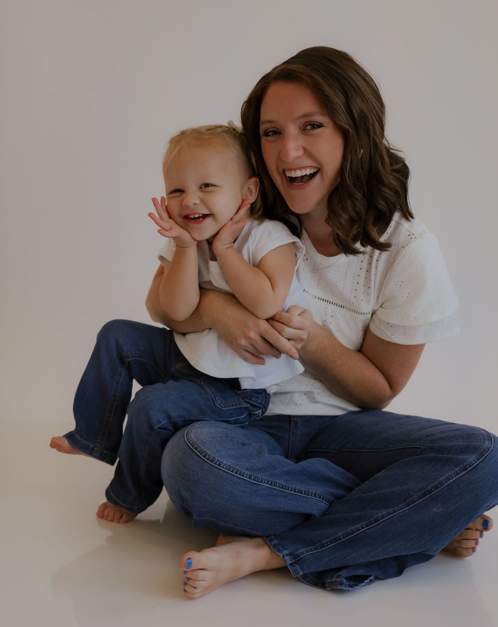 Joyful candid moment of adult and child laughing together while sitting on white floor.