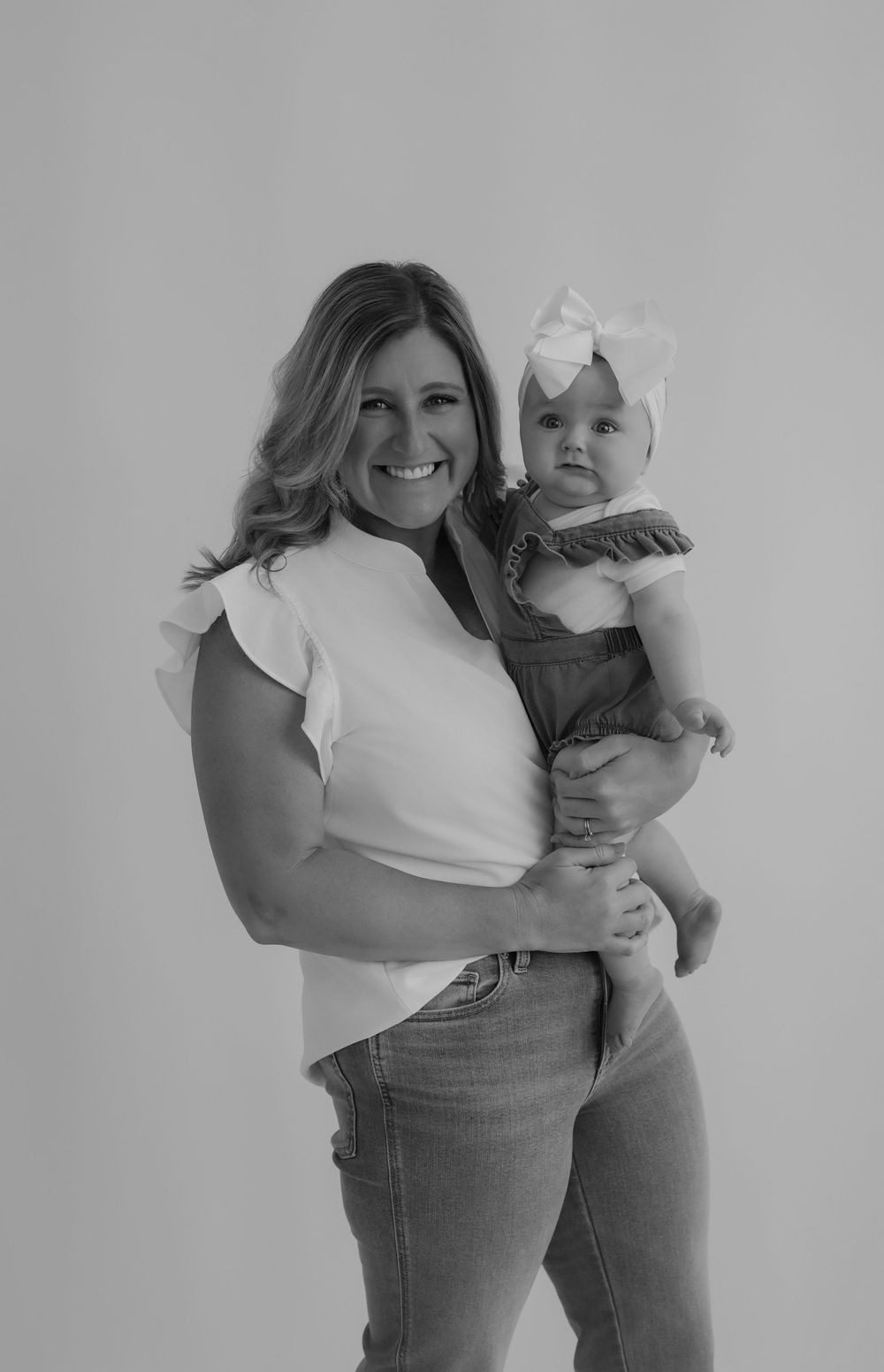 Studio portrait of adult and baby in coordinating white outfits against neutral background.