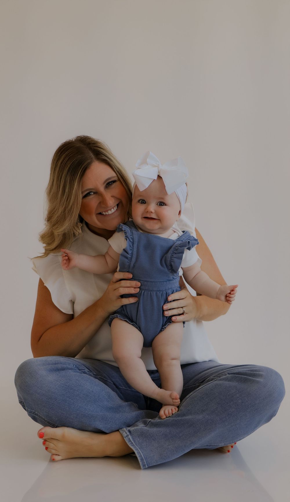Candid portrait of adult and baby in matching white and blue outfits sitting on floor.