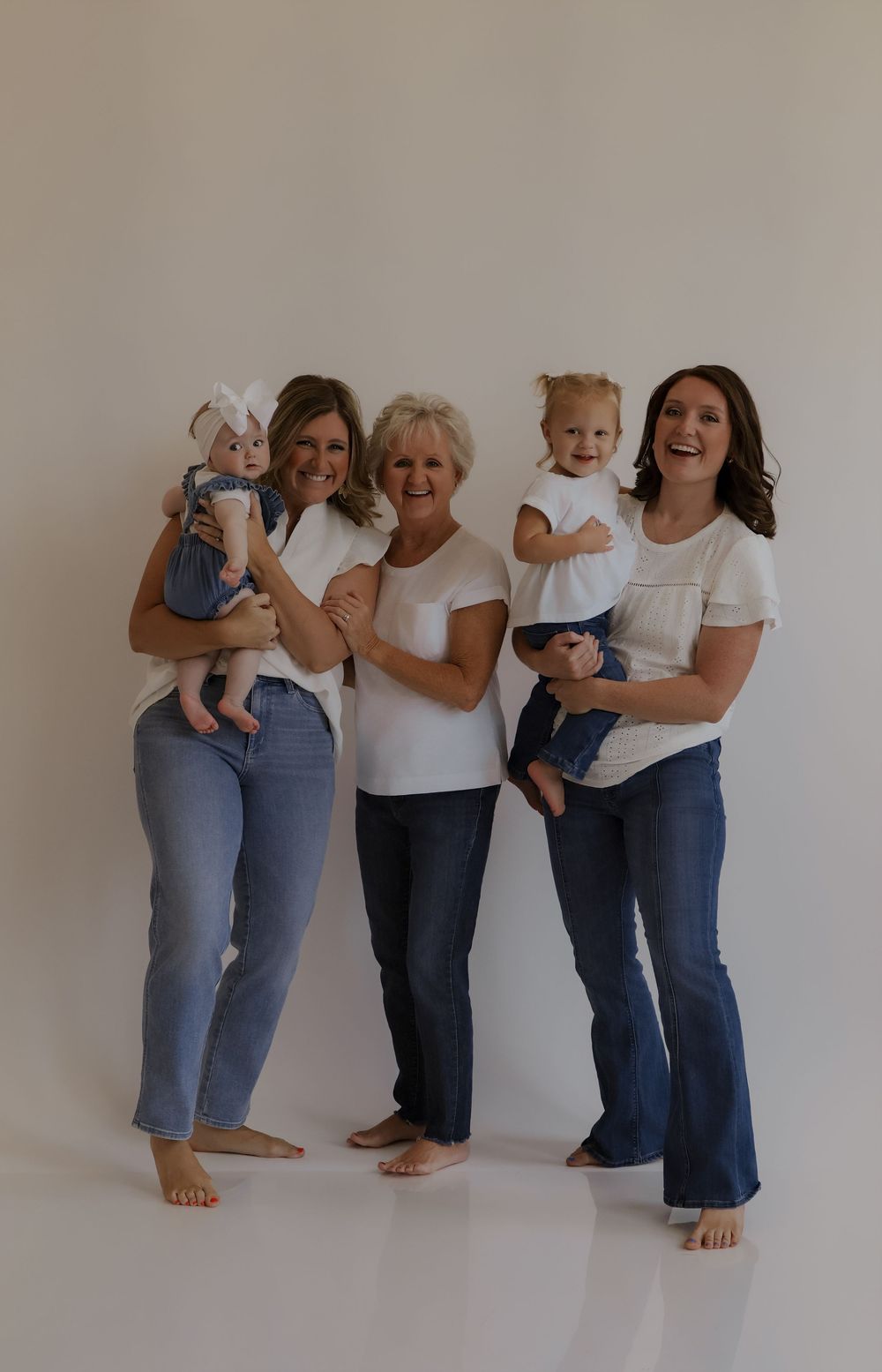 Four people in matching white tops and jeans pose playfully against a neutral wall.