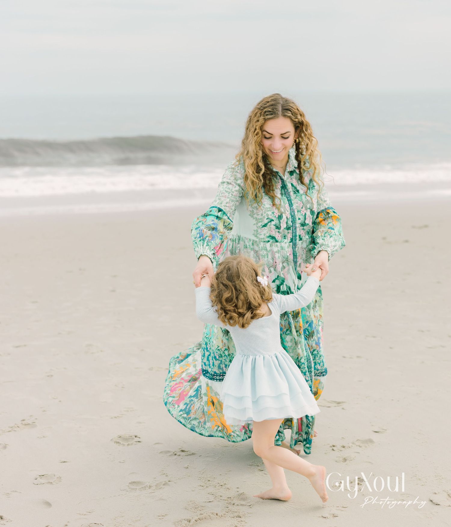Two people dance and twirl together joyfully on a misty beach, wearing coordinating floral dress and blue outfit.