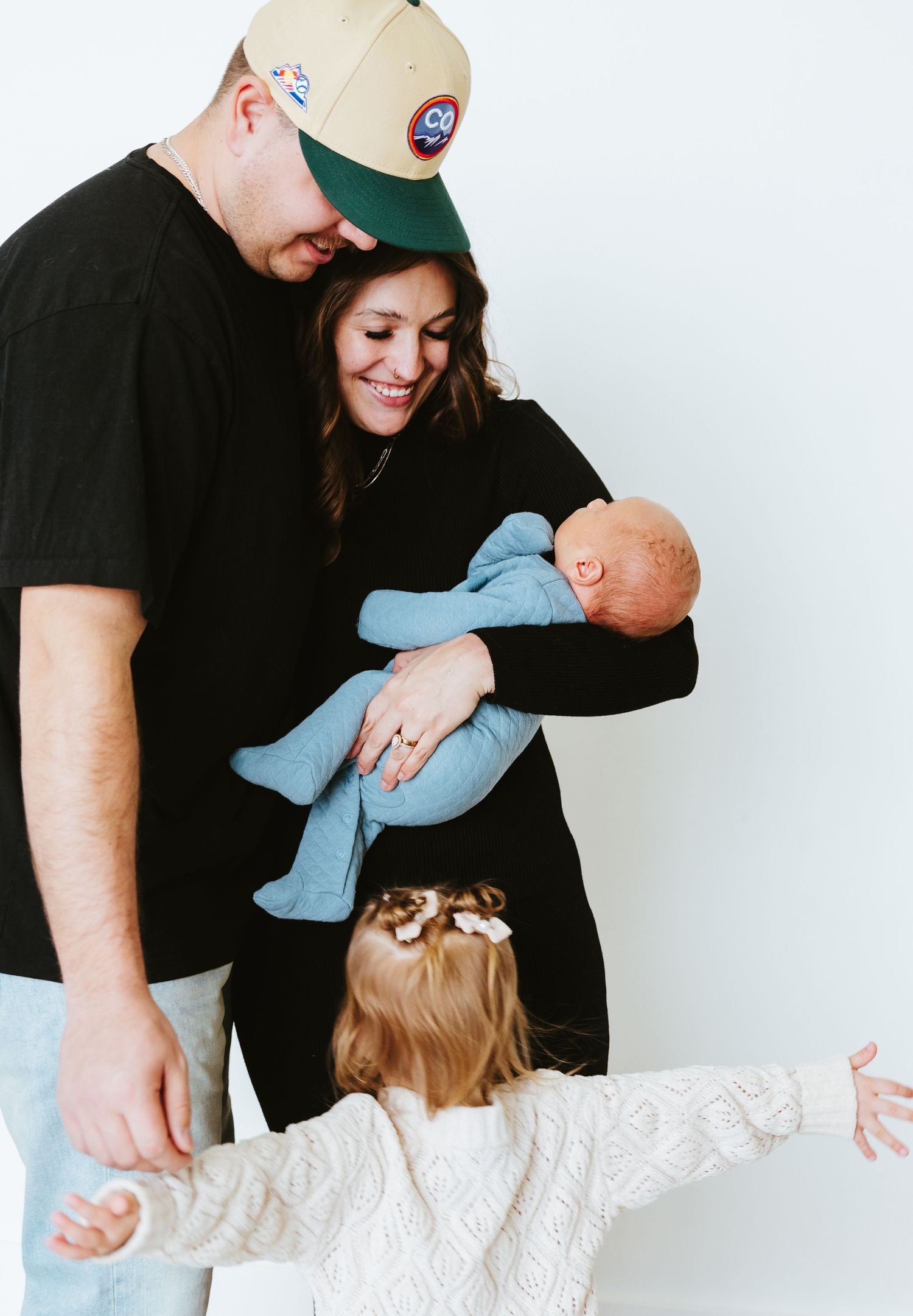 Family moment captured against white wall with infant in blue clothing.