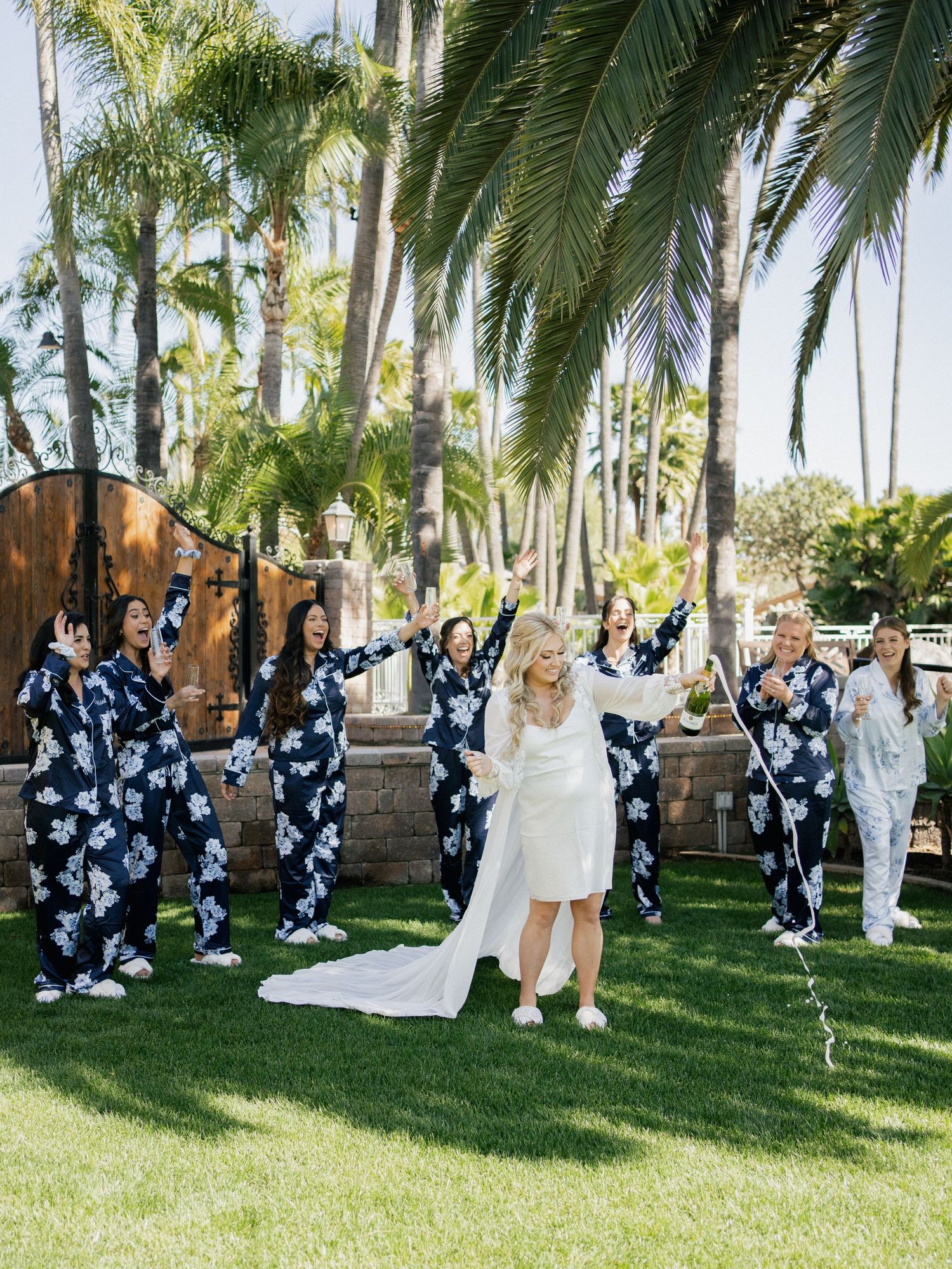 Group photo on a lawn with palm trees where people in matching floral print outfits celebrate around someone in white.