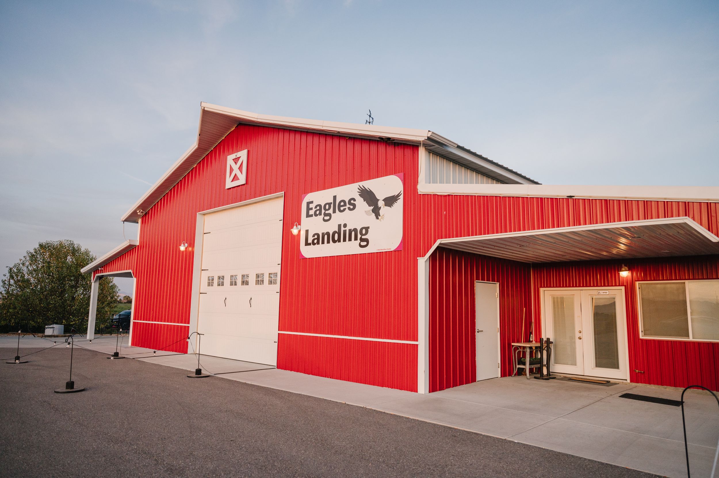 A bright red and white aircraft hangar building with 'Eagles Landing' signage stands against a blue sky.