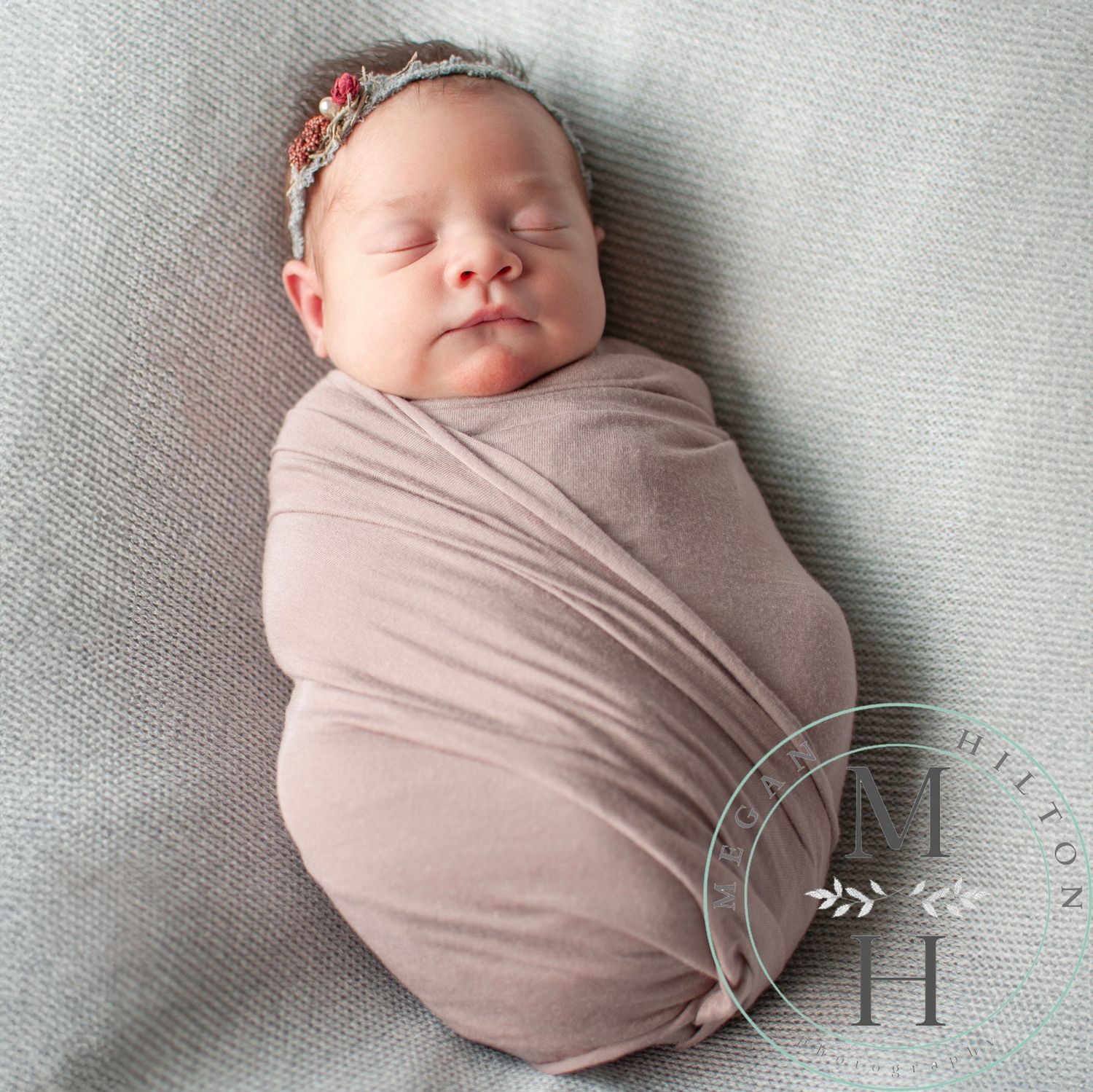 Photo of a peaceful sleeping newborn baby girl wrapped snugly in soft mauve swaddle blanket on textured gray background.