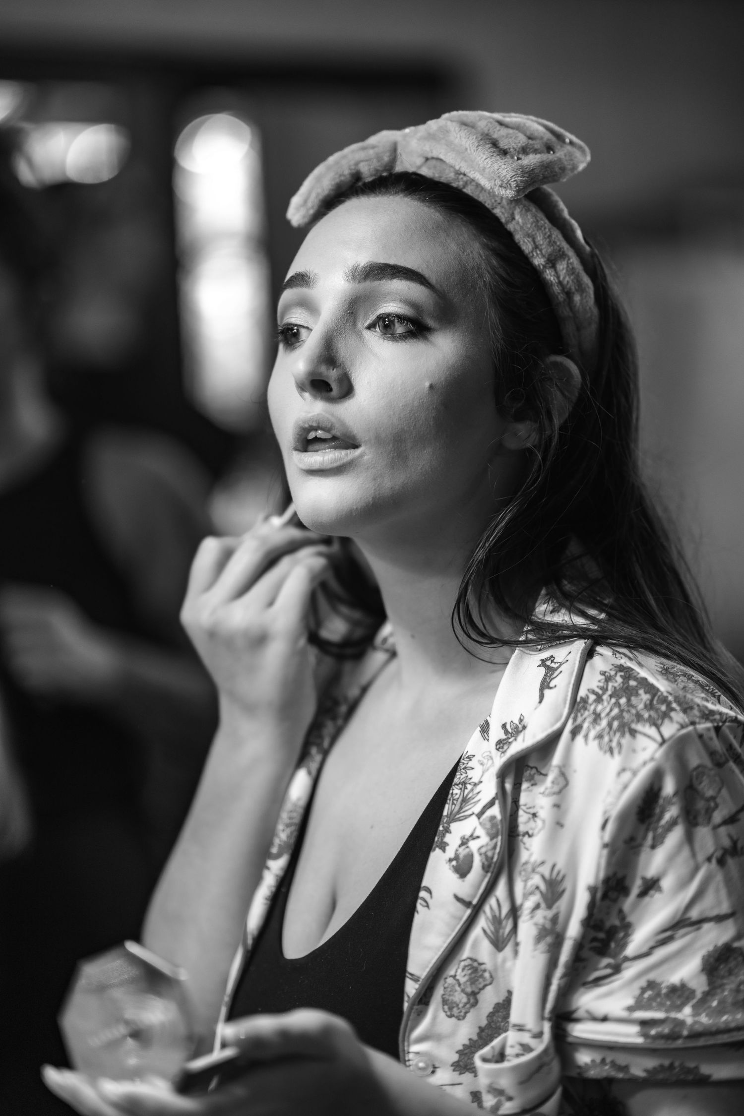 Black and white portrait of someone in a floral robe and headscarf looking pensively upward while touching their face.