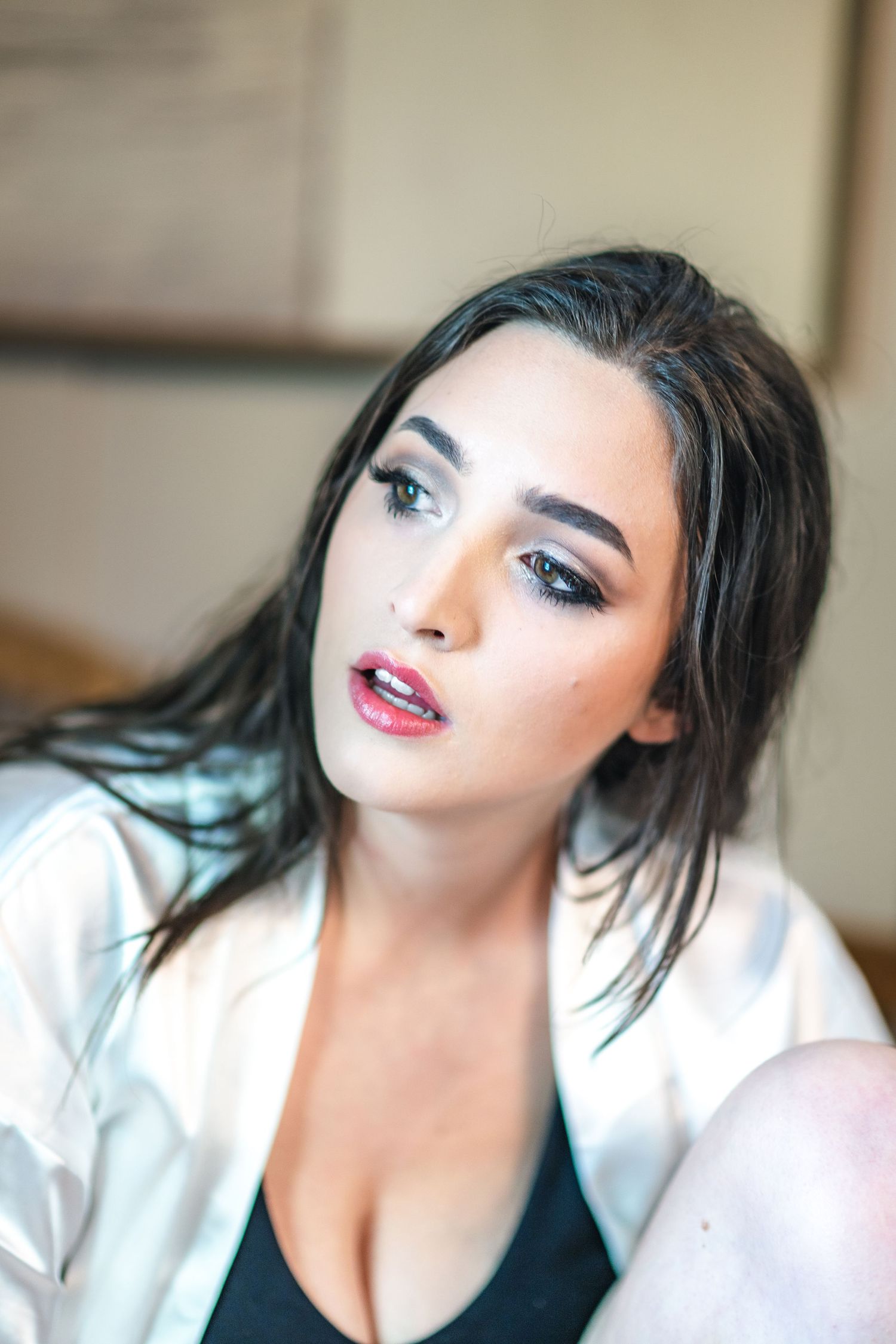 A close up beauty portrait showing dramatic makeup with red lips and smoky eyes wearing a white button up shirt.